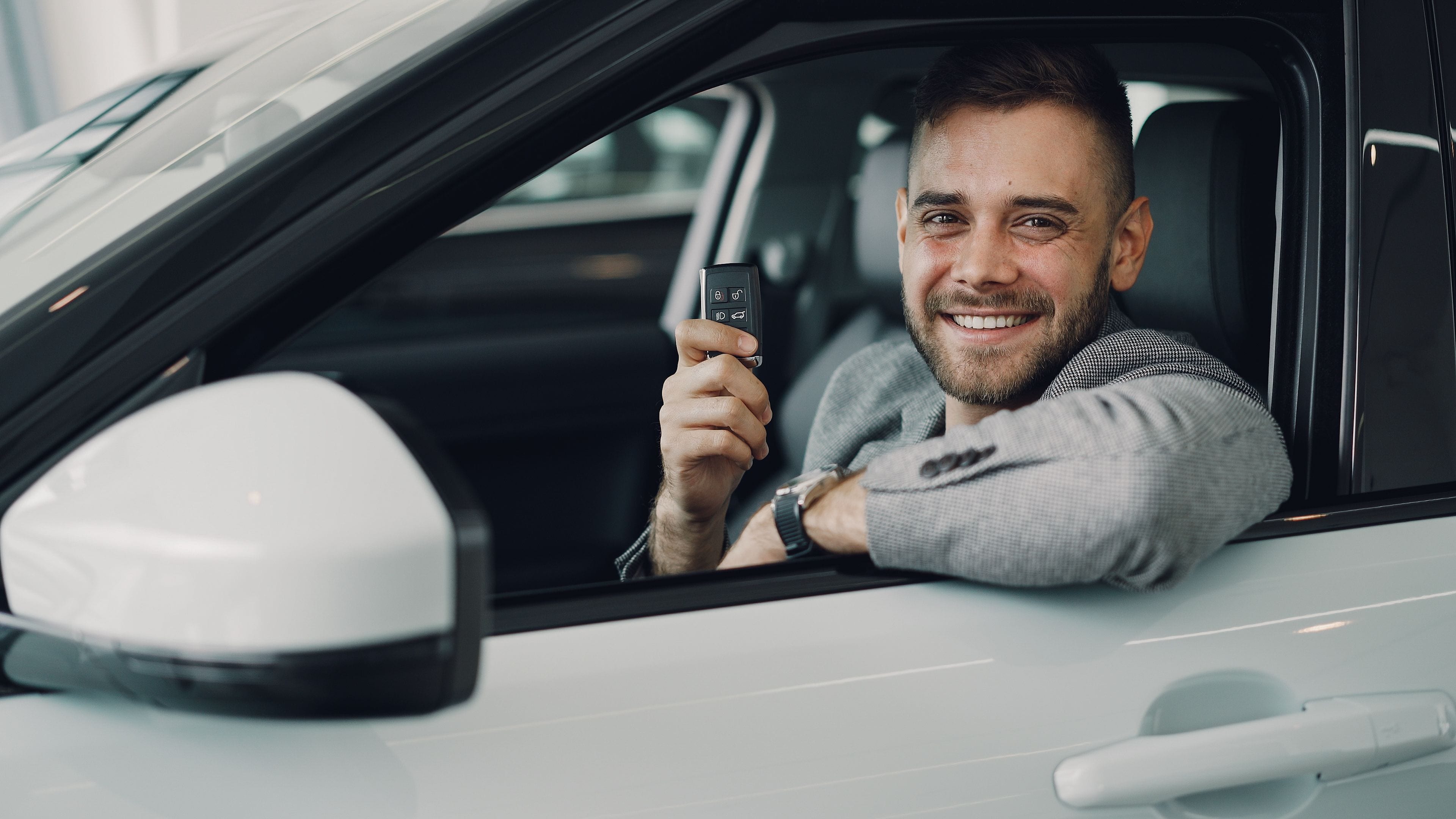 A customer sitting in the driver's seat of a white car, holding the keys